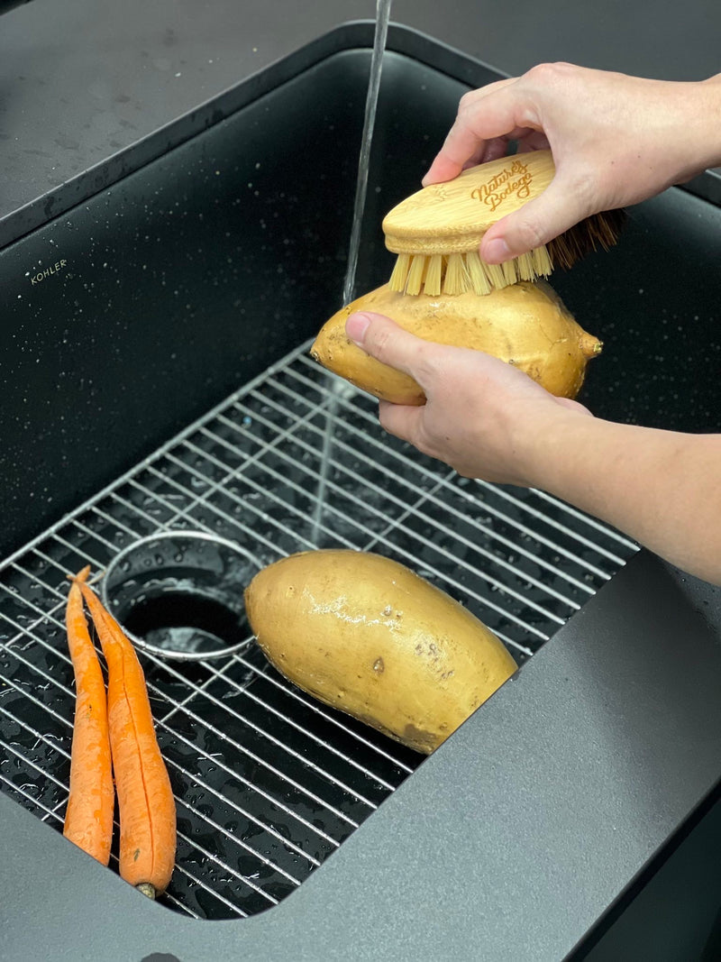 bamboo wooden vegetable brush cleaning a potato and carrots in the sink