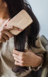 brunette brushing hair with wooden bamboo brush with wooden bristles. plastic free. zero waste. compostable. eco friendly